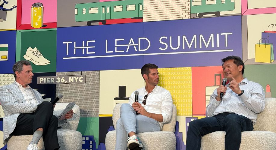 The Lead Summit, Pier 36, NYC. Three people on stage, two holding microphones, bright graphic background.