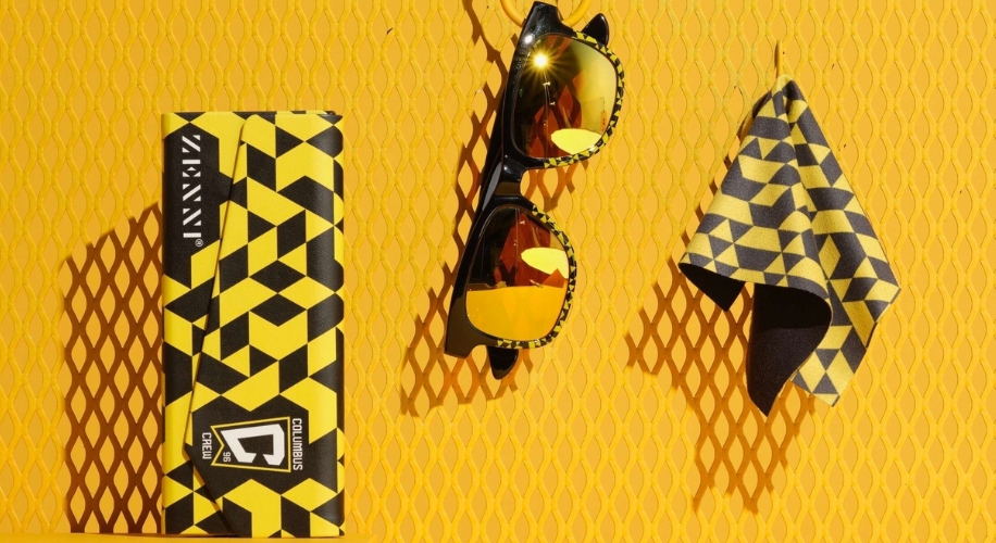 Yellow and black geometric pattern ZLensy sunglasses packaging, sunglasses with reflective lenses, and cleaning cloth.