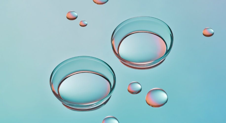 Two transparent contact lenses with reflective surfaces floating above a teal background with water droplets.