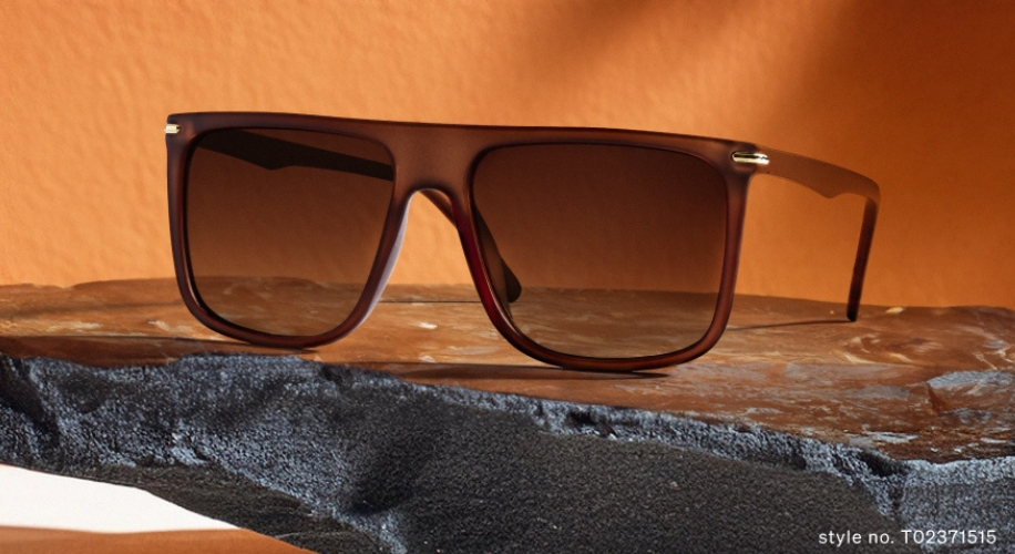 Sunglasses with dark gradient lenses on a textured stone surface. Style no. T02371515.