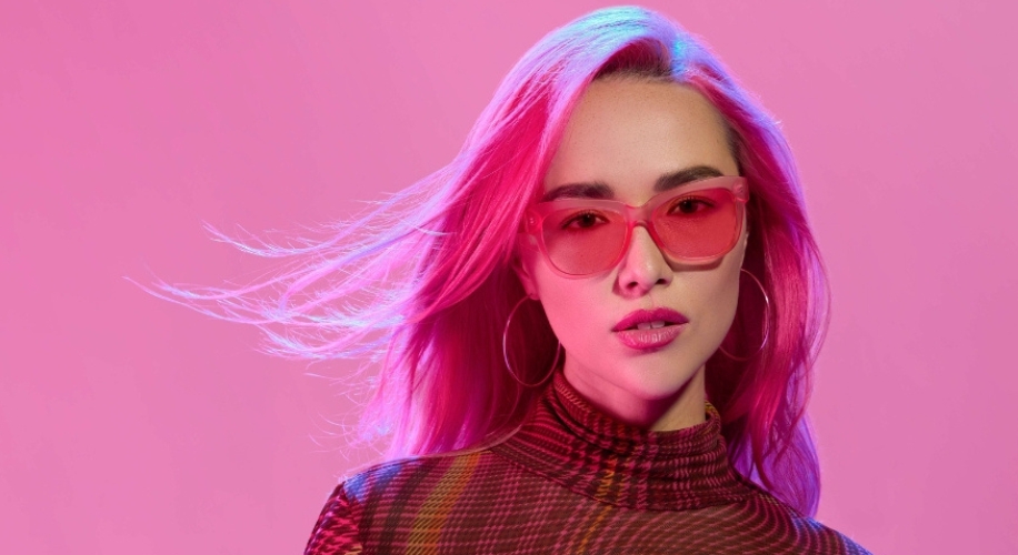 Woman with pink hair wearing pink-tinted sunglasses and a checkered turtleneck sweater.