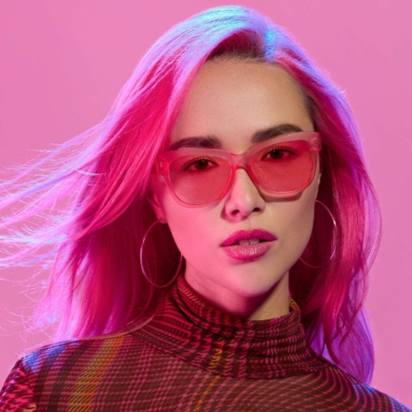 Woman wearing pink sunglasses and a plaid high-neck shirt with vibrant pink hair styled elegantly.