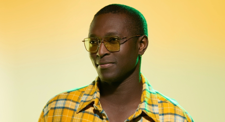 Man wearing yellow-tinted glasses and a yellow plaid shirt with open collar.