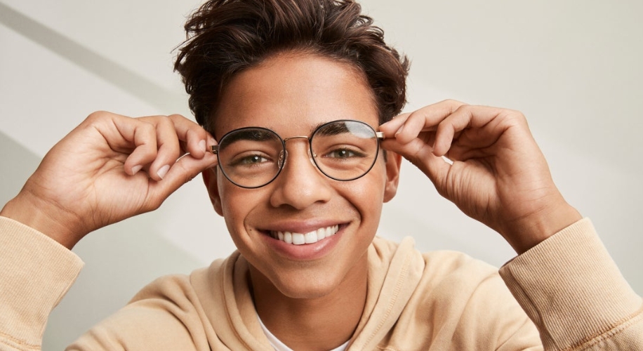 Teen smiling, wearing thin-frame eyeglasses and a beige hoodie.