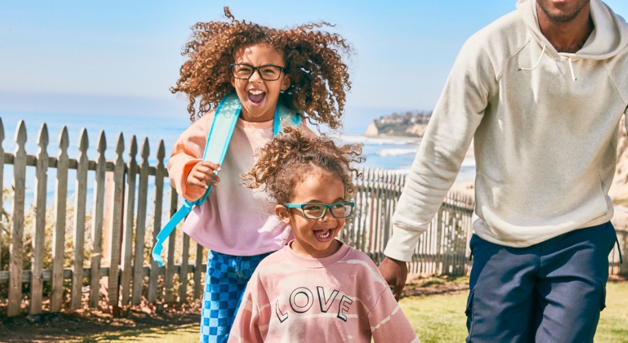 Two children wearing colorful glasses and sweatshirts, with the younger one&#039;s shirt reading &quot;LOVE.&quot;