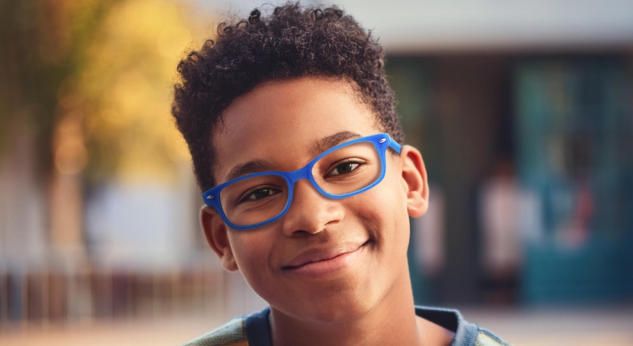 Boy wearing blue-framed eyeglasses, smiling at the camera.