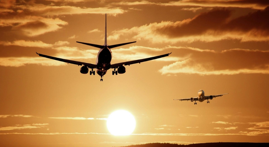 Two airplanes flying towards sunset with cloudy sky backdrop.