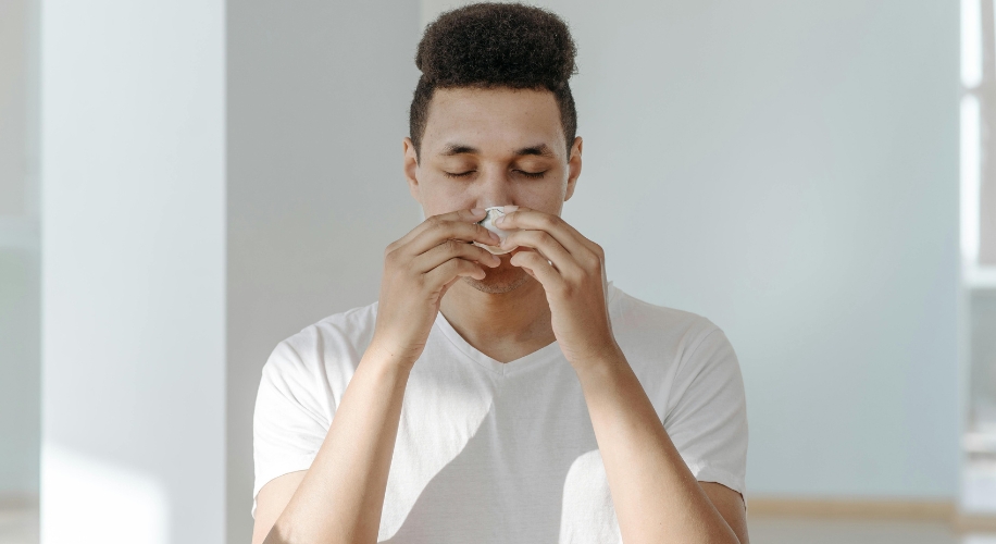 Person in a white shirt blowing their nose into a tissue.