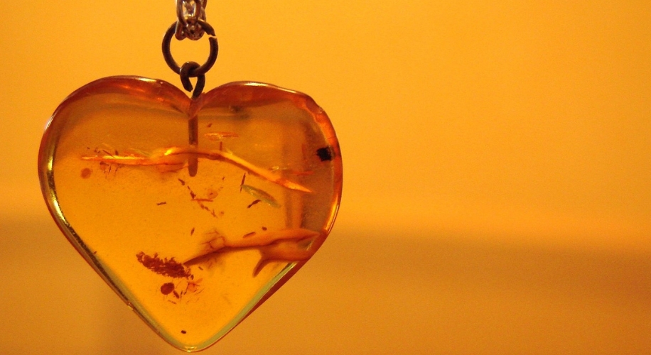 Amber heart-shaped pendant with inclusions, suspended by a small metal loop and chain.