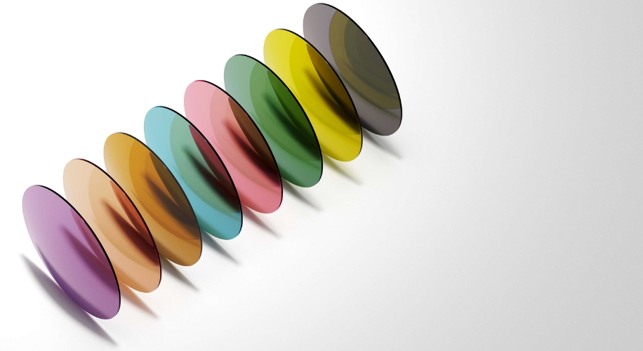 Colorful, translucent optical lenses arranged in a neat row, ranging from purple to dark gray.