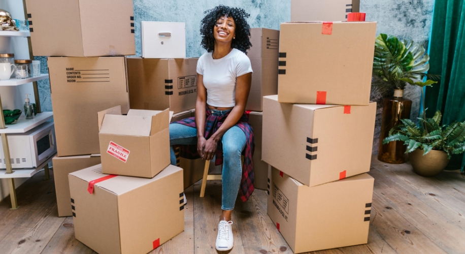 Woman sitting among stacked cardboard boxes with red tape. One box is labeled &quot;FRAGILE.&quot;