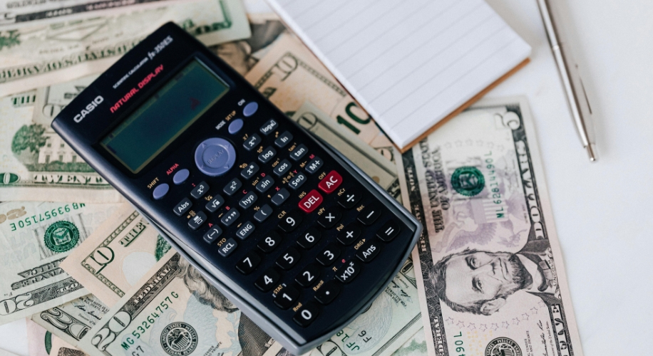 CASIO scientific calculator on mixed U.S. dollar bills, notebook, and pen in the background.