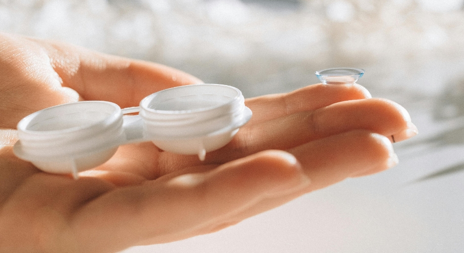 Contact lens and white contact lens case held in an open hand.