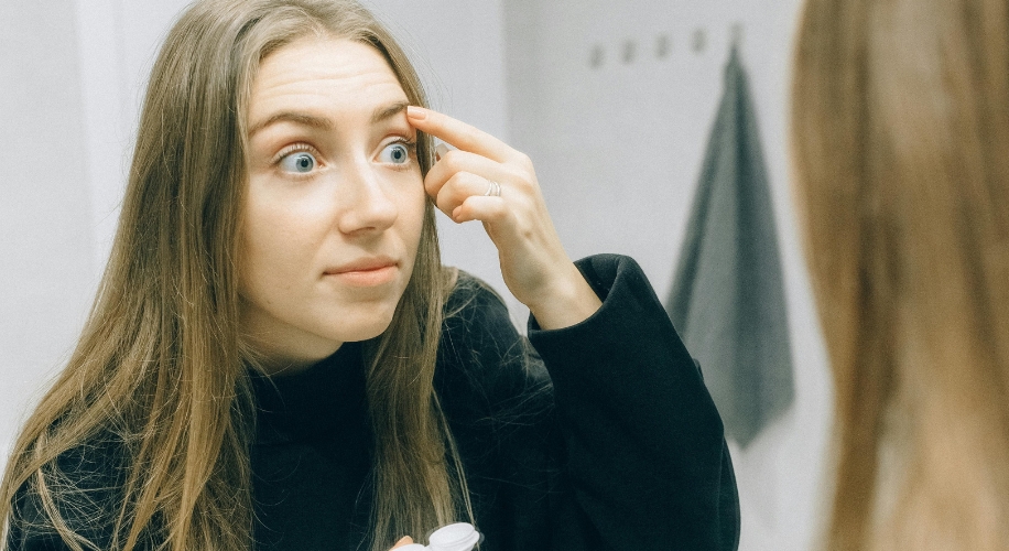 Woman applying contact lens while looking in the mirror.