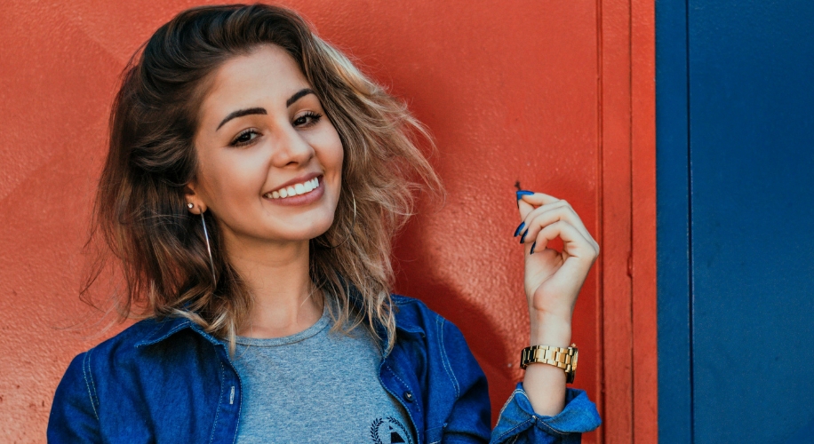 Smiling person wearing a denim jacket and gray shirt, holding a blue item.