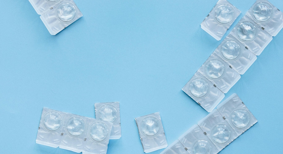 Contact lenses in clear blister packs arranged on a light blue background.