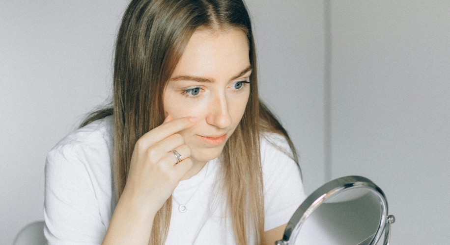 Woman examining her face in a round handheld mirror.