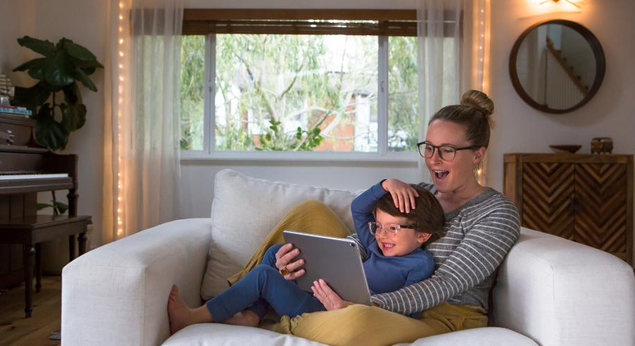 Woman and child sitting on a white couch, smiling and looking at a tablet.