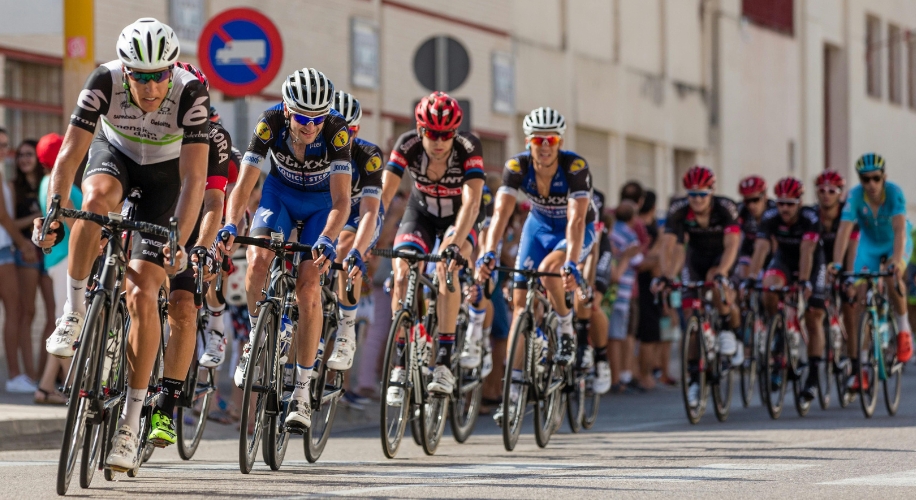 Cyclists in a competitive race, each wearing team jerseys and helmets, riding in a tight formation.