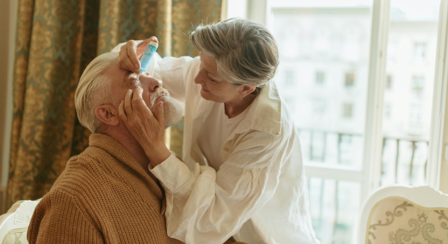 Older woman assisting older man with eyedrops.