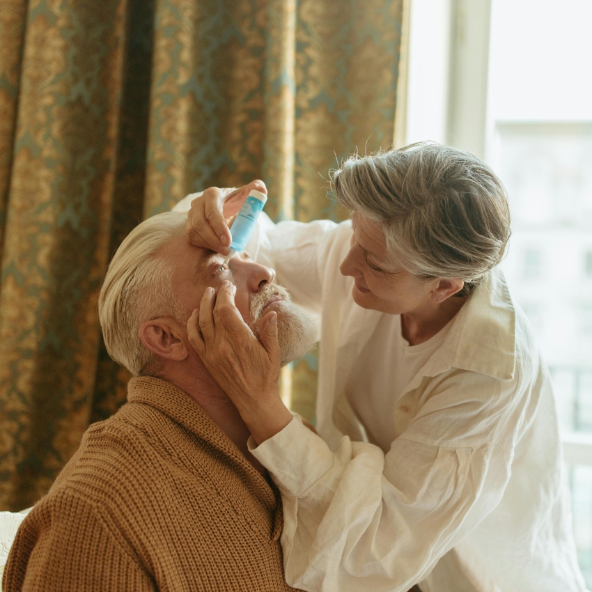 Woman administering eye drops to an elderly man’s eye.