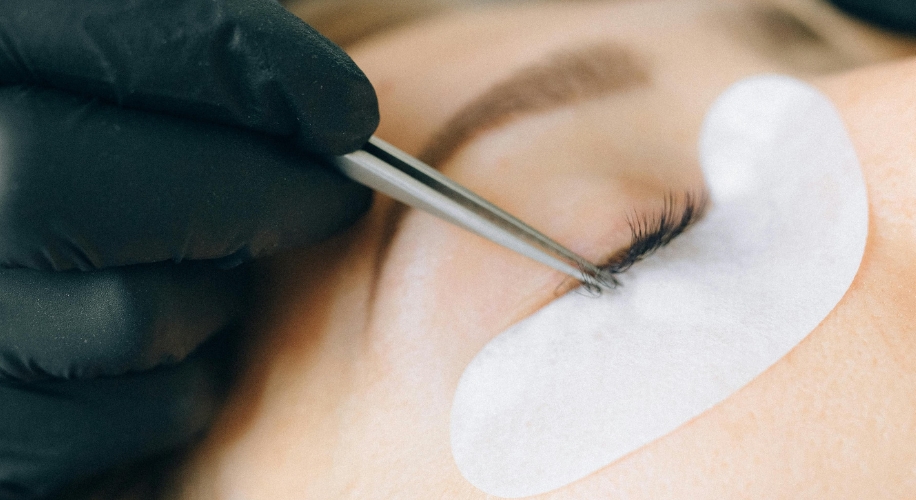 Applying eyelash extensions using tweezers, eye shield pad covering lower lashes.