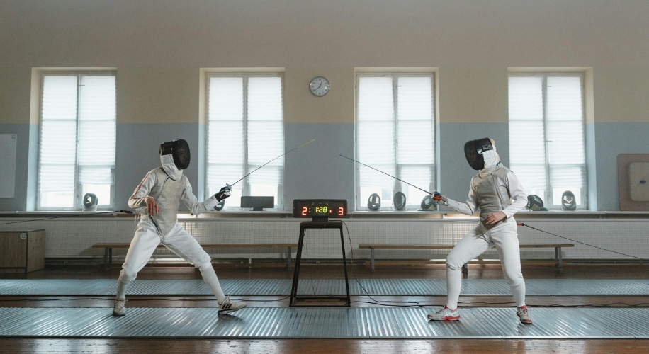 Two fencers in white uniforms and black masks engaged in a duel, with a scoreboard showing 2-3 and 1:28.