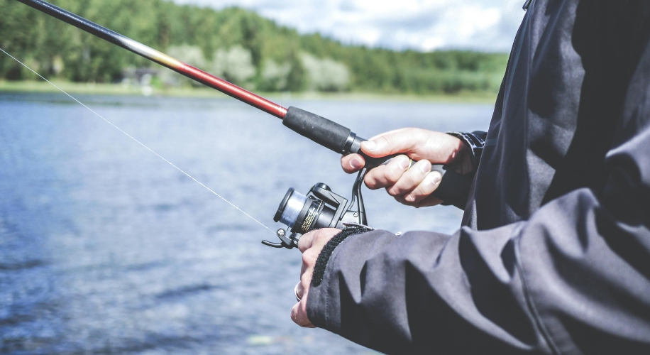 Man holding a fishing rod and reel by a lakeside.