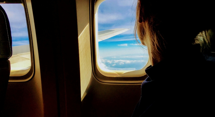 Person looking out an airplane window at a wing and blue sky.