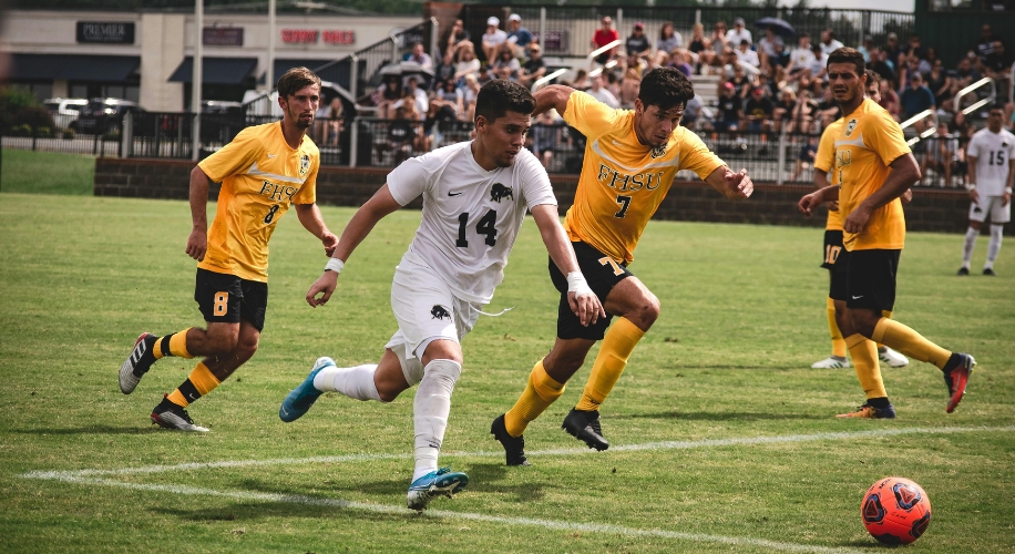 Soccer players in action; one in white jersey number 14, others in yellow jerseys with numbers 7 and 8.