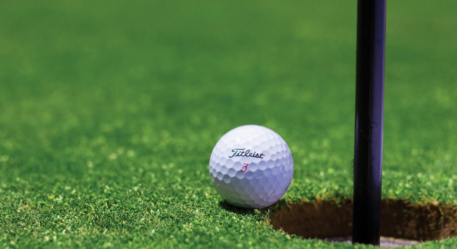 Titleist golf ball number three next to a hole on green grass.