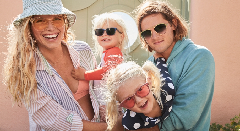 Family wearing stylish sunglasses; two adults with two children, all smiling and having fun.