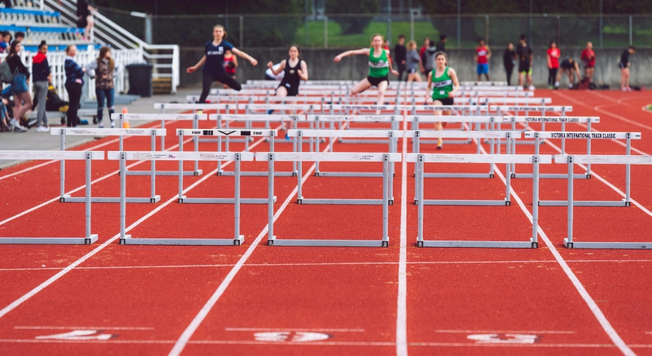 Athletes competing in hurdle race on red track, Victoria International Track Classic hurdles.