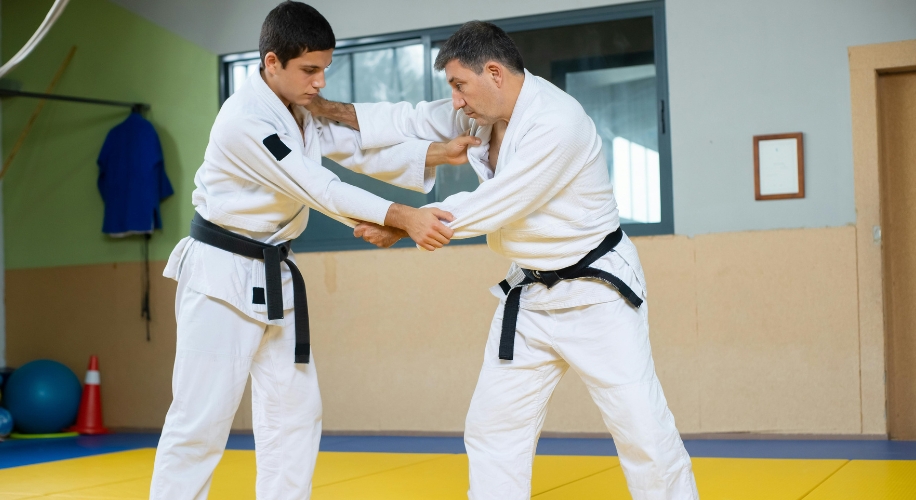 Two men practicing judo in white gis and black belts in a dojo.