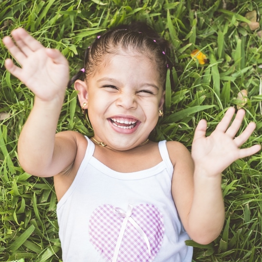 Smiling child with hands up wearing a white tank top with a purple checkered heart design.