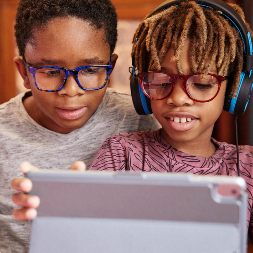 Two children wearing glasses and headphones looking at a tablet screen.