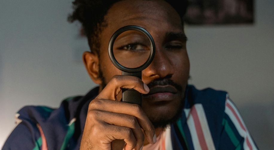 Man holding a black magnifying glass near his right eye.