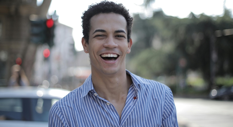 Person wearing a blue and white striped shirt, smiling broadly outdoors.