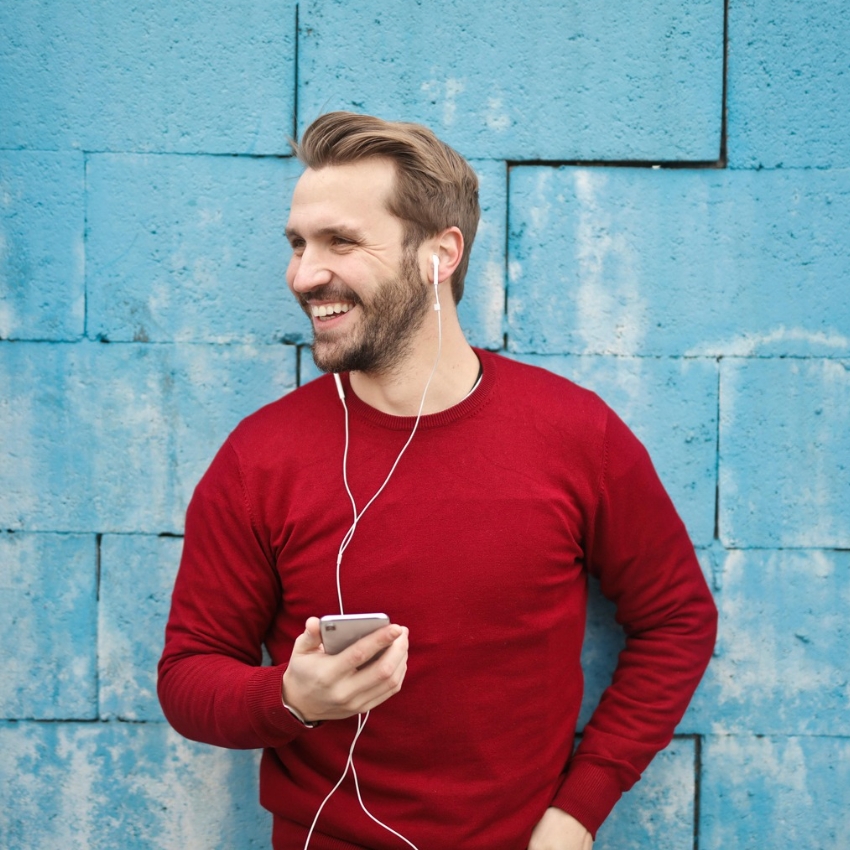 Man in red sweater using white earphones connected to a smartphone.