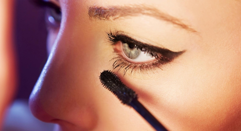 Mascara being applied to eyelashes of a person&#039;s eye with black eyeliner.