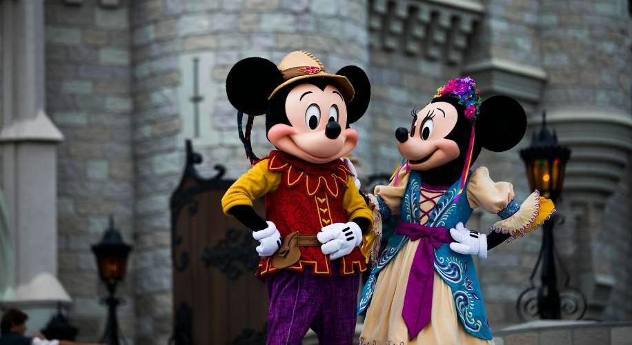 Mickey Mouse and Minnie Mouse wearing colorful, themed costumes, with a cheerful expression.