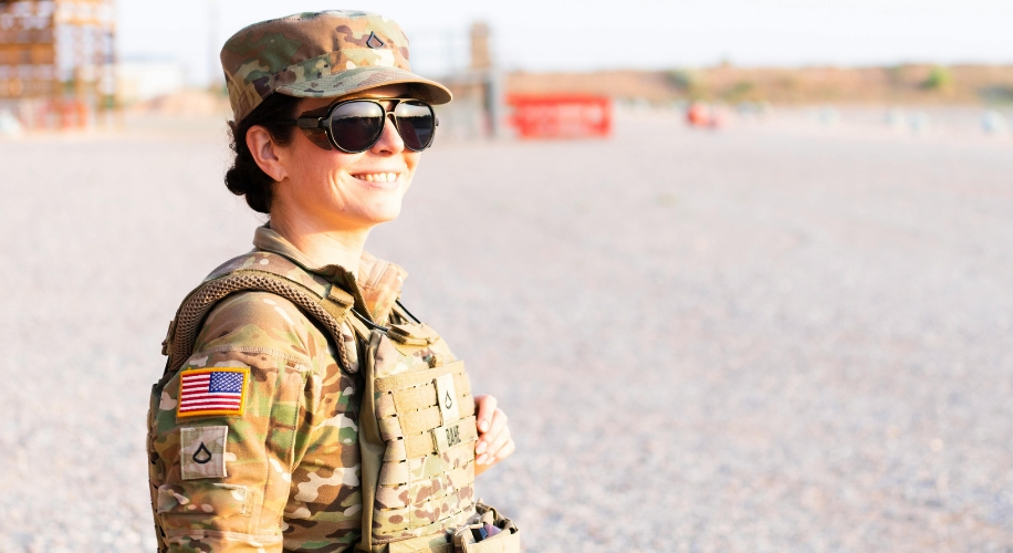 Army soldier in uniform and sunglasses, standing outdoors and smiling, with a flag patch on the sleeve.