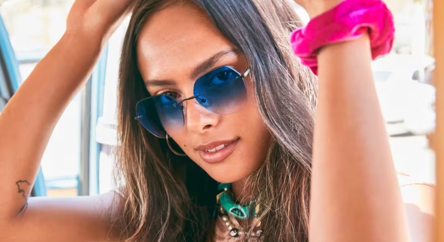 Woman wearing gradient blue sunglasses and a pink scrunchie on her wrist, adjusting her hair.