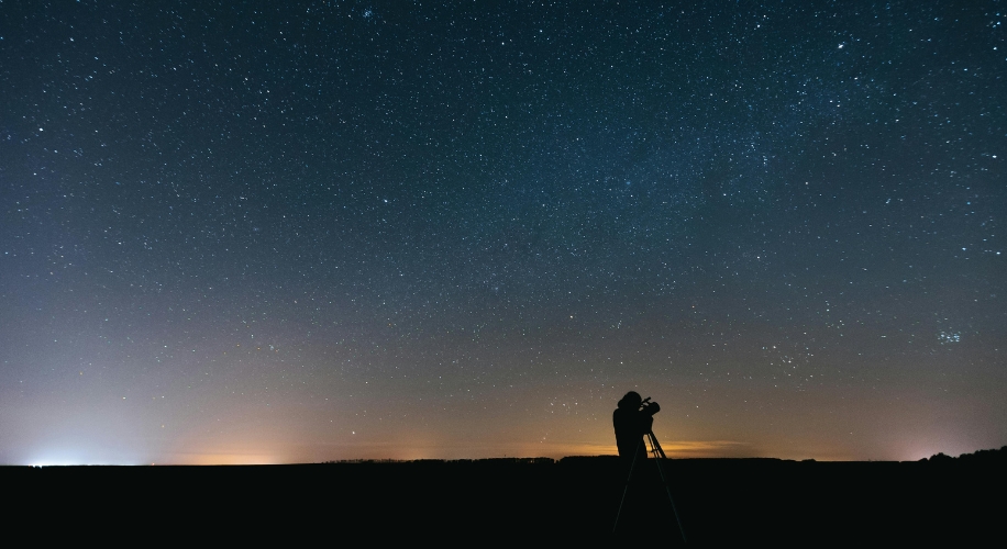 Person using a telescope under a starry night sky.