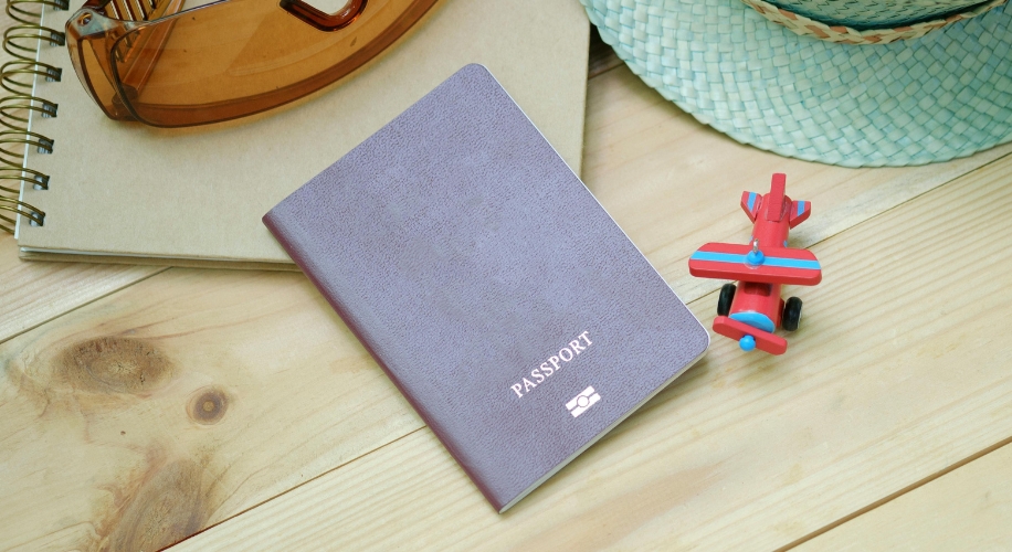 Purple passport next to a red toy airplane on a wooden surface.