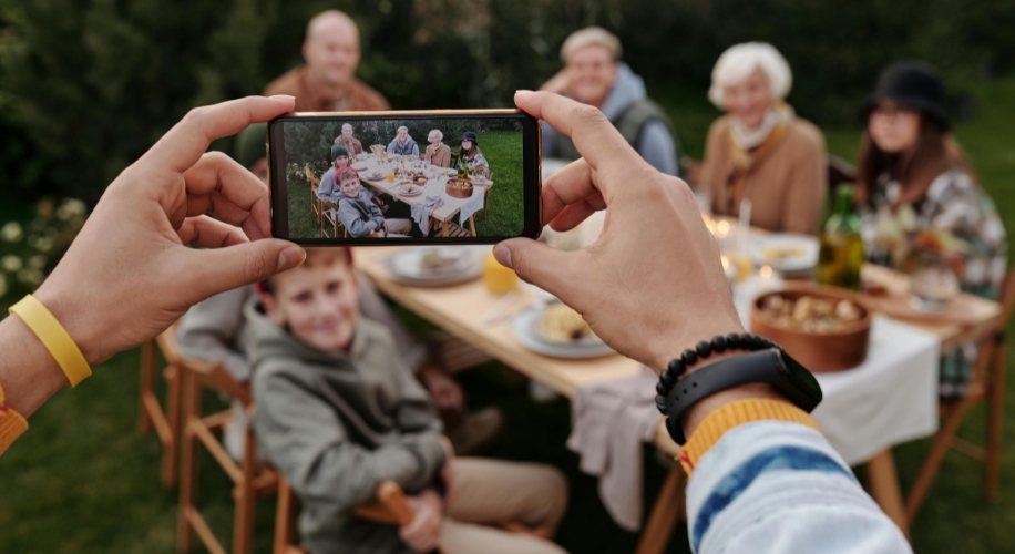 Hands holding a smartphone capturing a group of people around an outdoor dining table.