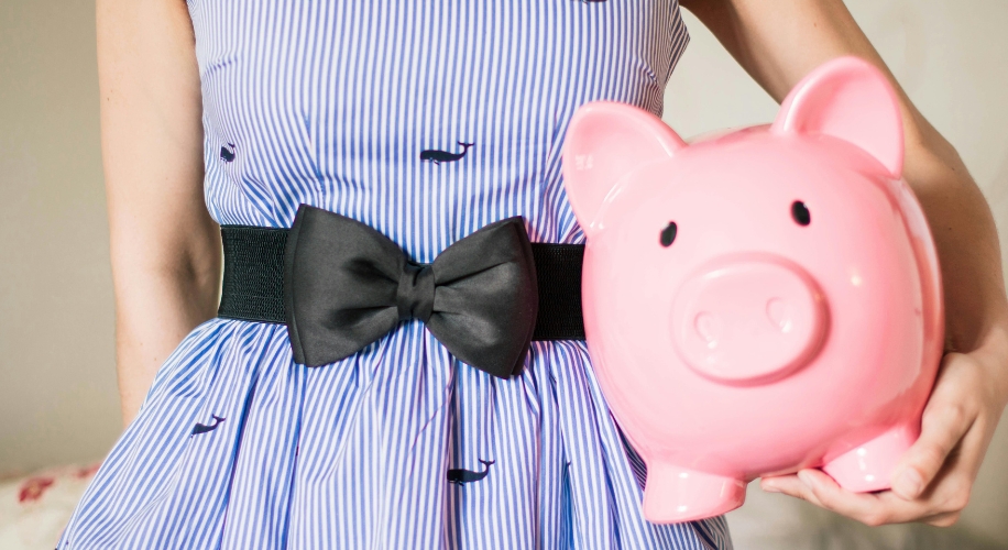 Person holding a pink piggy bank. Person wearing a blue striped dress with whales pattern and black belt with bow.