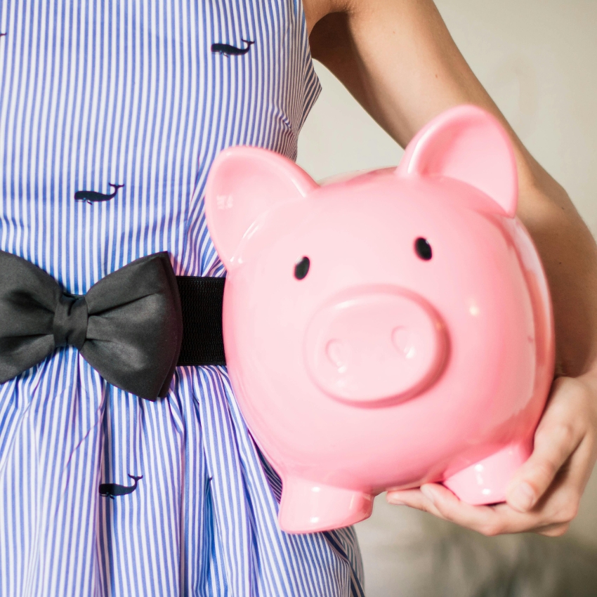 Pink ceramic piggy bank being held by a person wearing a blue and white striped dress with a black bow.