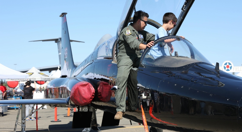 Two people examining a sleek black aircraft with its canopy open.