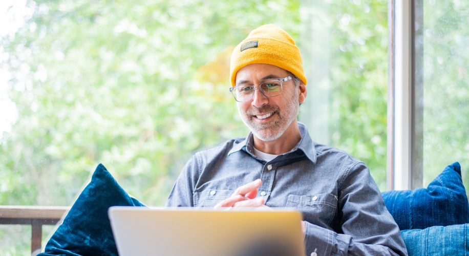 Man in a yellow beanie using a laptop while sitting on a blue couch.